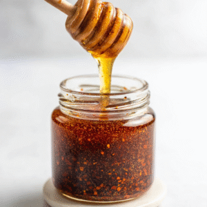 Wooden honey dipper dripping spicy hot honey into a glass jar